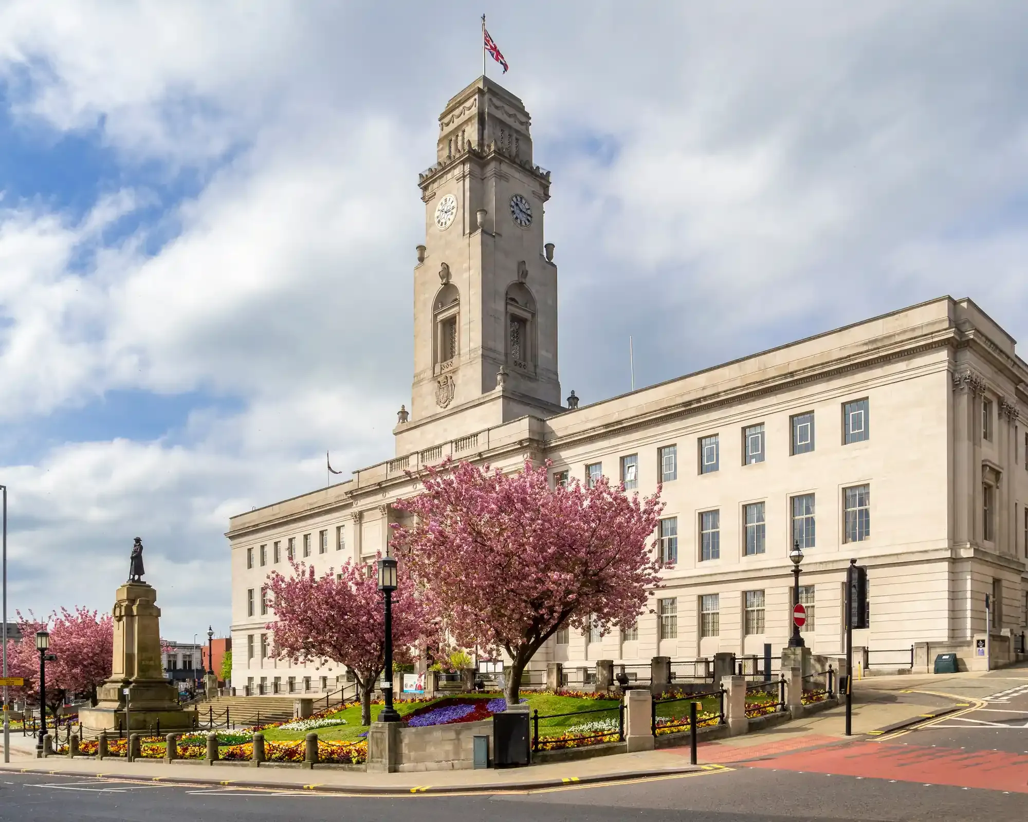 Barnsley Town Hall's white stone clock tower above flowering cherry trees and the war memorial in the town centre.