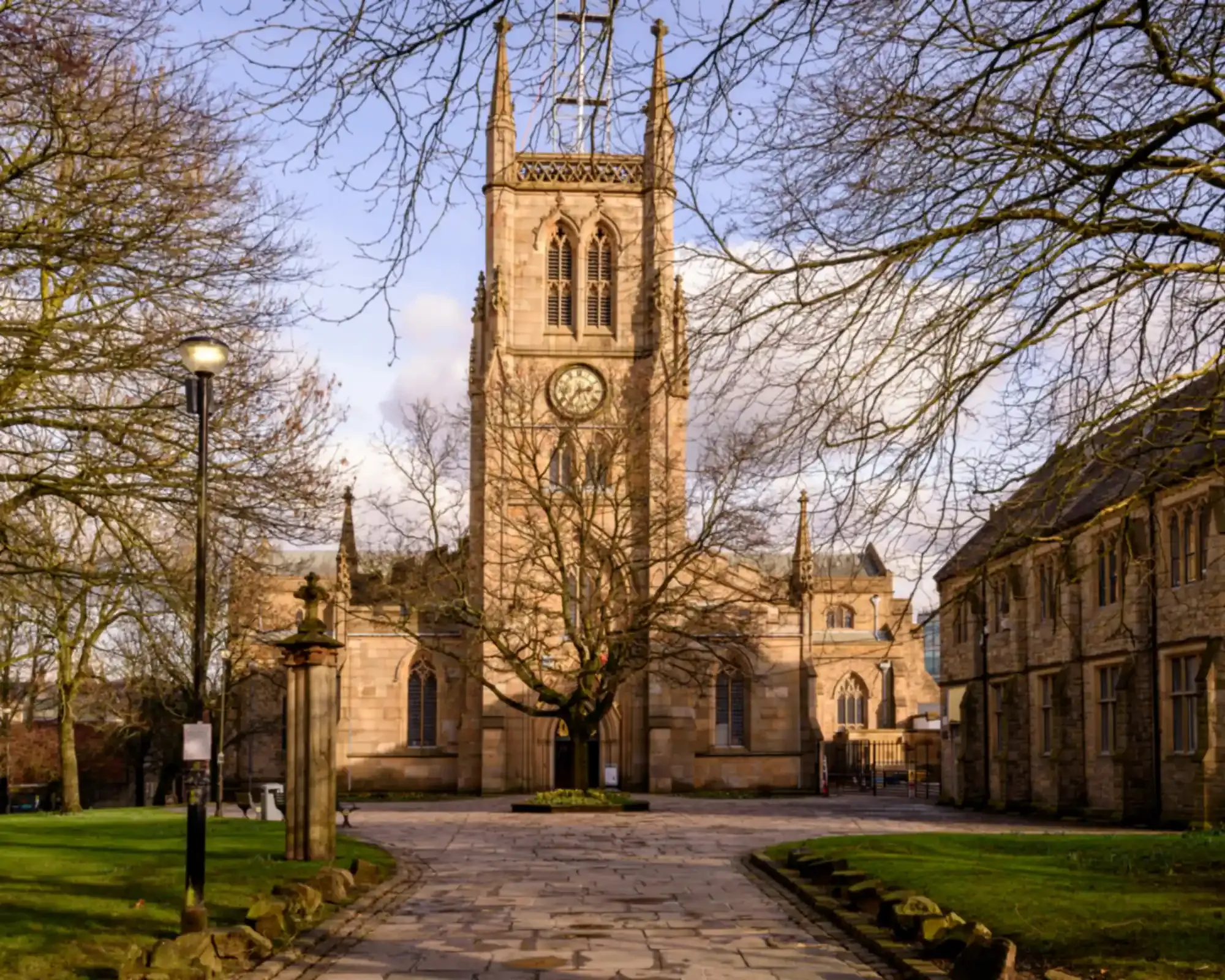 The sandstone tower of Blackburn Cathedral, seen through bare winter trees across the cathedral grounds.