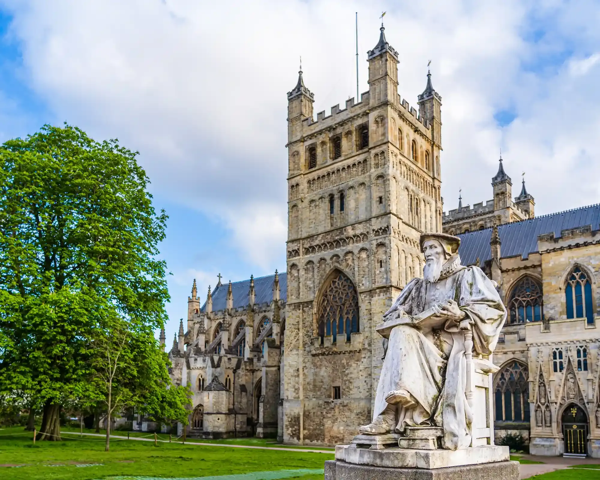 Exeter Cathedral's Norman tower and Cathedral Green, with the white marble statue of Richard Hooker in the foreground.