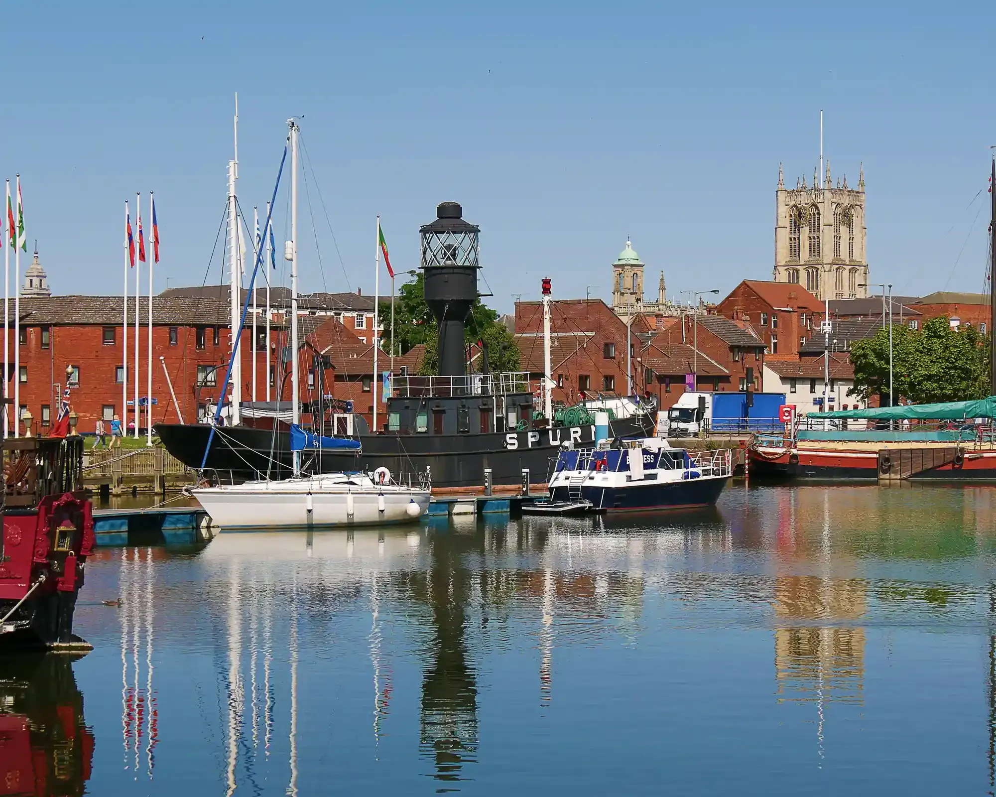 Hull Marina with the historic Spurn Lightship and moored boats, and the tower of Hull Minster rising above red-brick buildings.