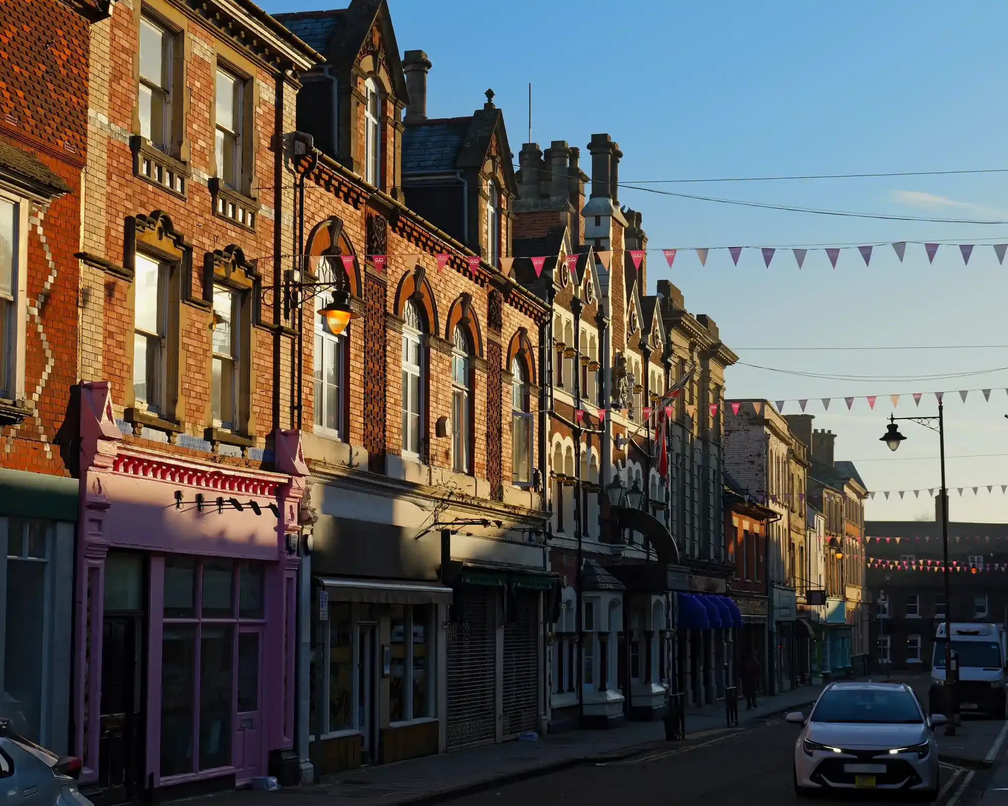 Ornate Victorian brick shopfronts and bunting along a street in Swindon Old Town, lit by low winter sun.