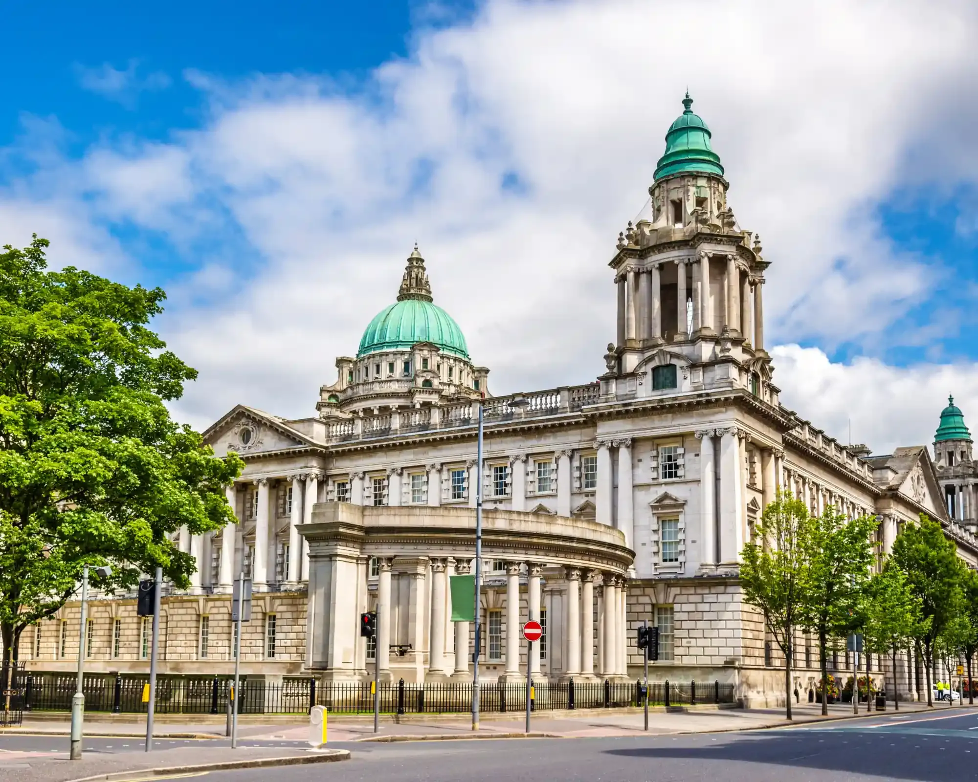 Belfast City Hall’s copper dome and corner towers under a blue sky.