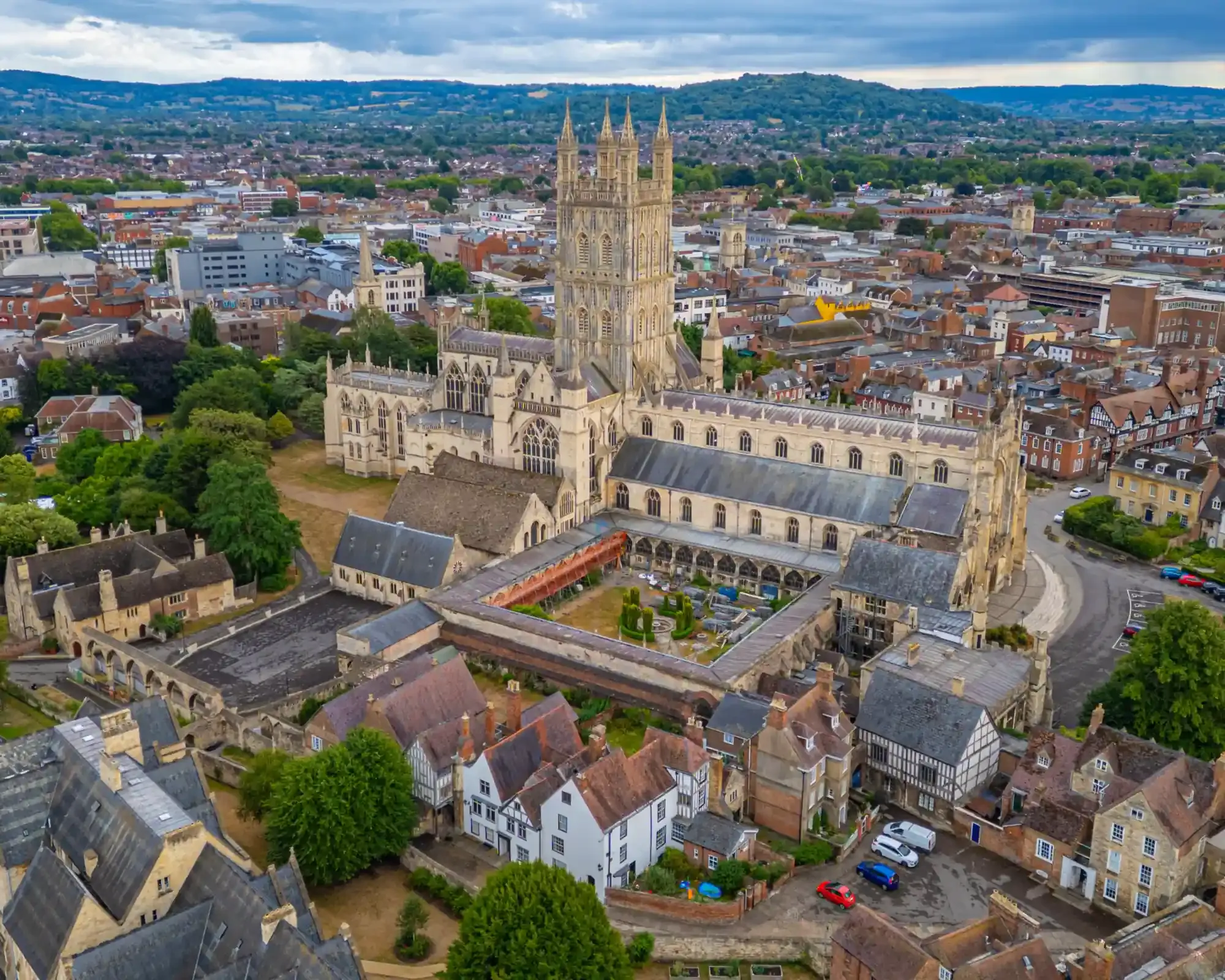 Aerial view of Gloucester Cathedral and its cloisters, with the city and Cotswold hills behind.