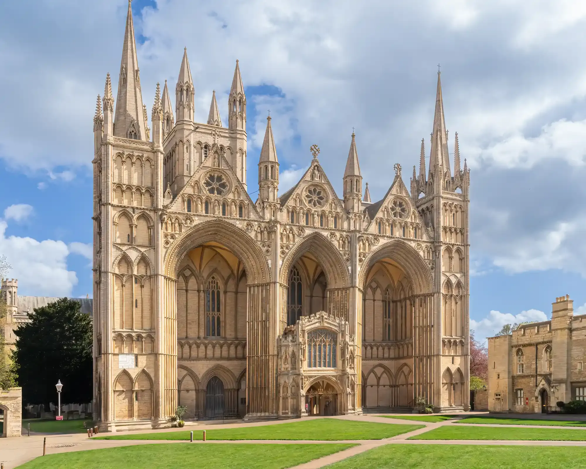 The west front of Peterborough Cathedral, with its three great arches and spires, under a blue sky.