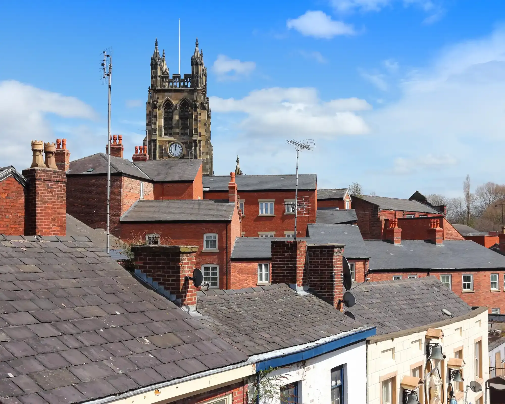 St Mary’s Church tower rising above red-brick rooftops and chimneys in Stockport town centre.